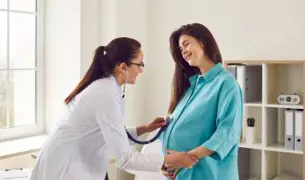 רופאה עם סטטוסקופ מקשיבה לעובר של אישה הריונית בכחול