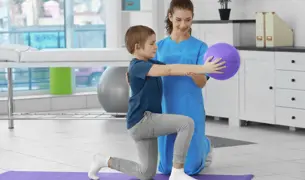 ילד מתרגל מודעות לגוף באמצעות שיטת אלבאום עם מטפלת בעזרת כדור קטן