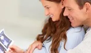 זוג יושבים מחובקים ומתבוננים בתמונות אולטרסאונד של תינוק