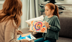 A girl shows a woman a drawing