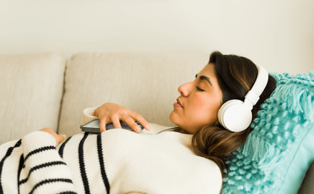 A woman is lying on the sofa and listening to music in headphones