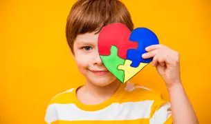 ילד קטן מחזיק לב בצבעים של מודעות לאוטיזם