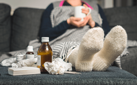 A woman who is not feeling well is holding a glass and next to the woman is medicine