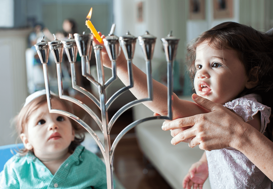 ילדה מדליקה נר חנוכה עם ליווי אחד ההורים