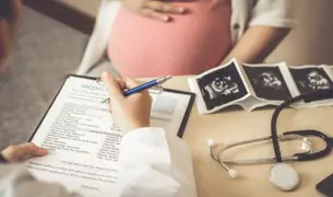 אישה הריונית יושבת מול הרופאה עם תמונות אולטרסאונד לידה וטופס