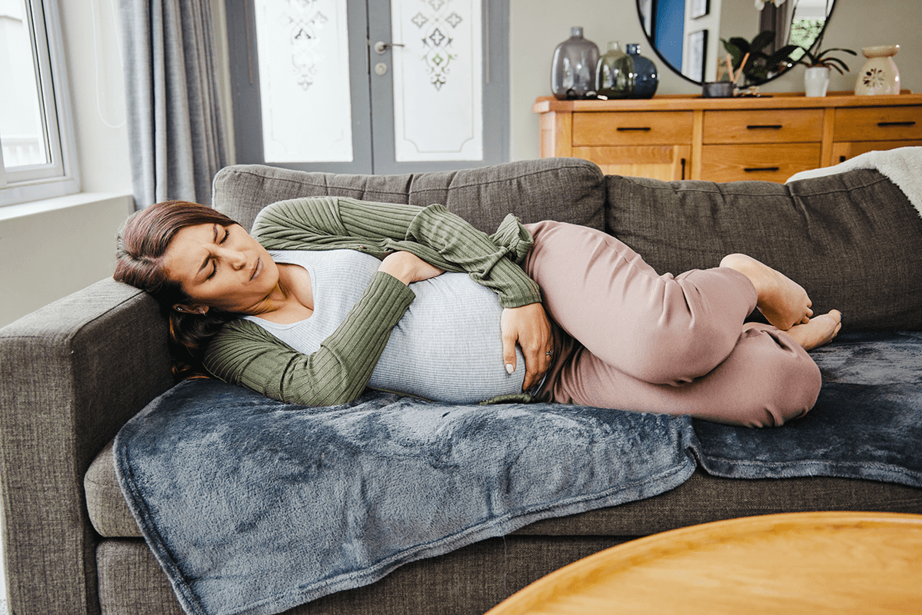 A woman holds her stomach and lies on the sofa