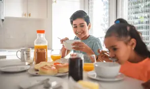 ילד מחייך תוך כדי שהוא מחזיק צלחת, מסתכל על אחותו שאוכלת בשולחן