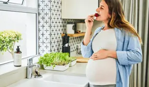 אישה בהריון עומדת ליד חלון המטבח ואוכלת דובדבן